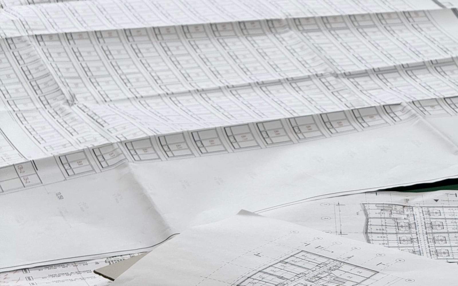 Architectural blueprints spread across a desk, sheets of floor plans layered over one another