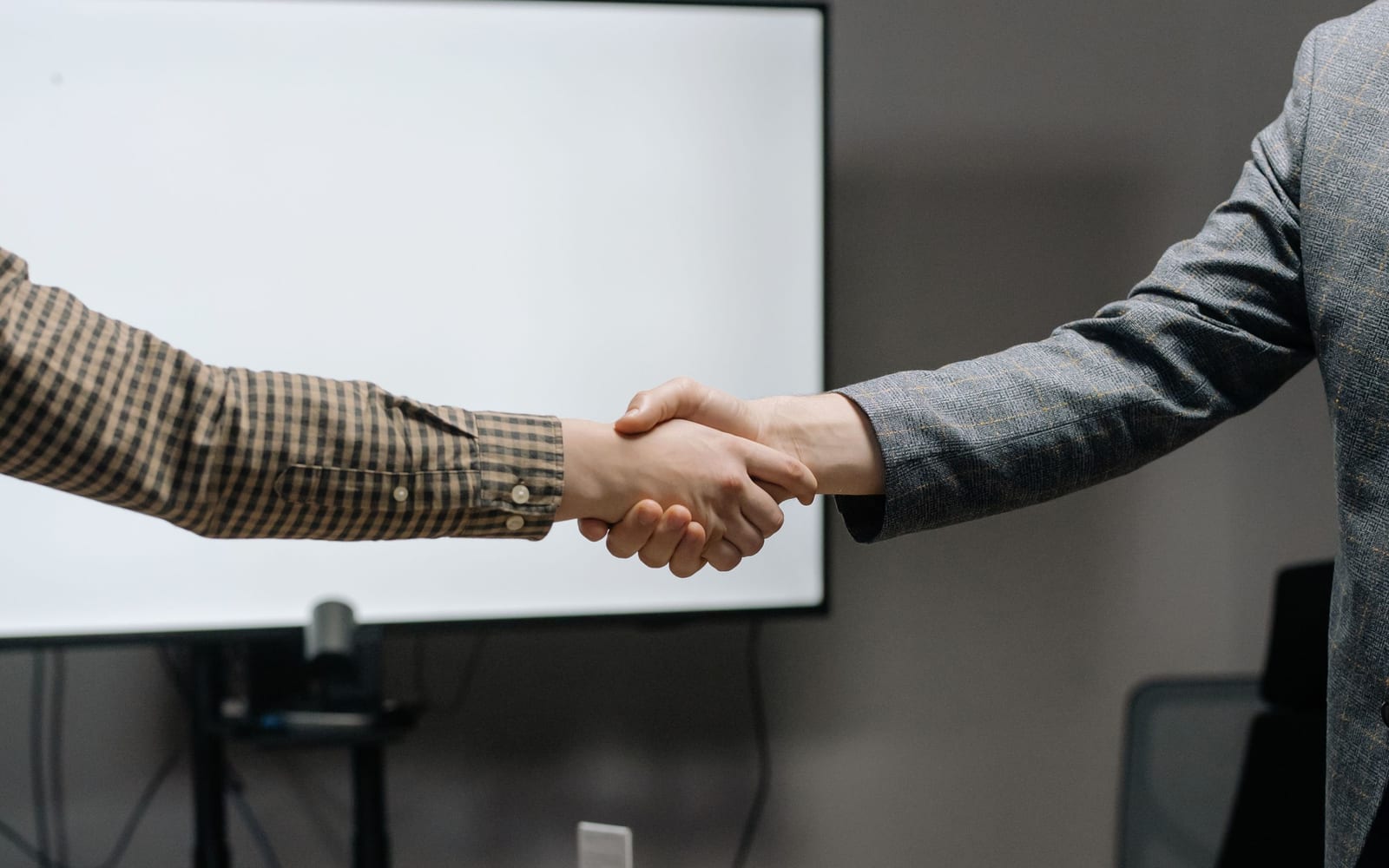 Two people shaking hands across a meeting room table